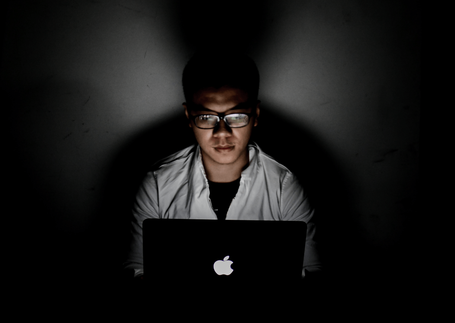 Man wearing glasses sitting in with laptop in the dark